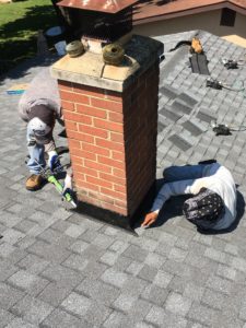 Roofers putting finishing touches on new aluminum flashing around roof chimney